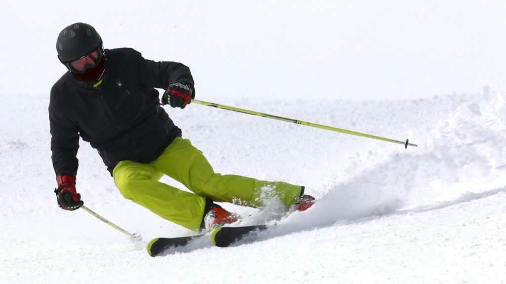 Wintersporter in actie op de piste met designer-skistokken in felgeel, toonbeeld van stijl en controle tijdens het skiën.