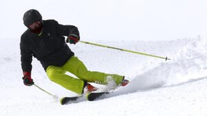 Wintersporter in actie op de piste met designer-skistokken in felgeel, toonbeeld van stijl en controle tijdens het skiën.