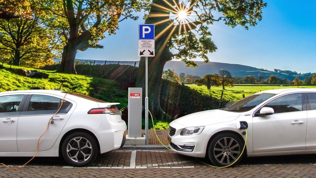 Twee witte elektrische auto's staan geparkeerd en laden op bij een laadpaal op een zonnige, landelijke locatie – perfect voor shortlease.