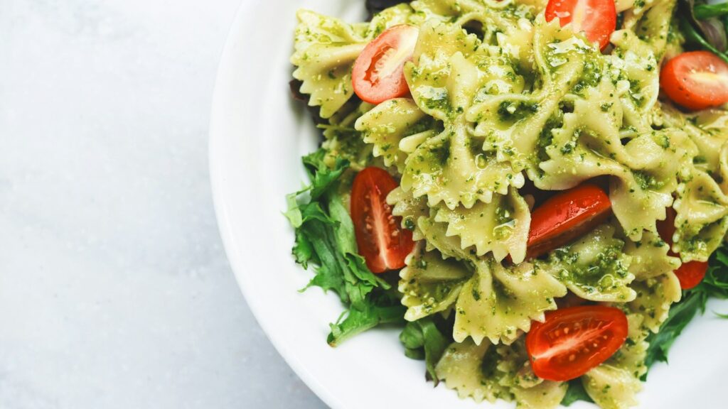 Luxe foodpakket met farfalle pasta in pesto, kerstomaatjes en verse rucola op een wit bord