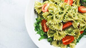 Luxe foodpakket met farfalle pasta in pesto, kerstomaatjes en verse rucola op een wit bord