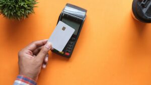 Hand houdt een betaalkaart bij een luxe betaalterminal voor contactloze betaling op een oranje achtergrond