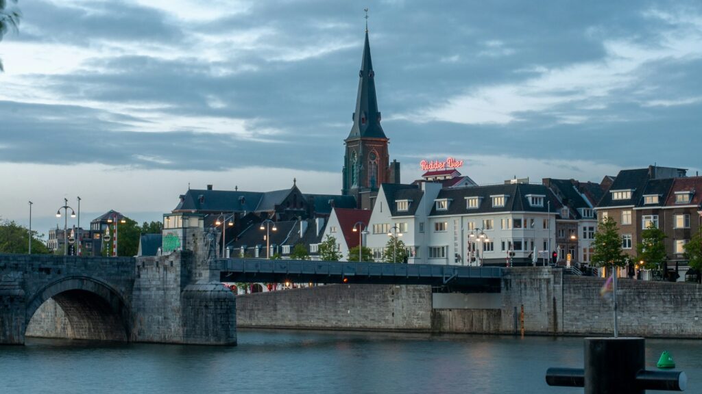 Uitzicht op de historische binnenstad van Maastricht met brug, kerktoren en sfeervolle verlichting bij schemering.