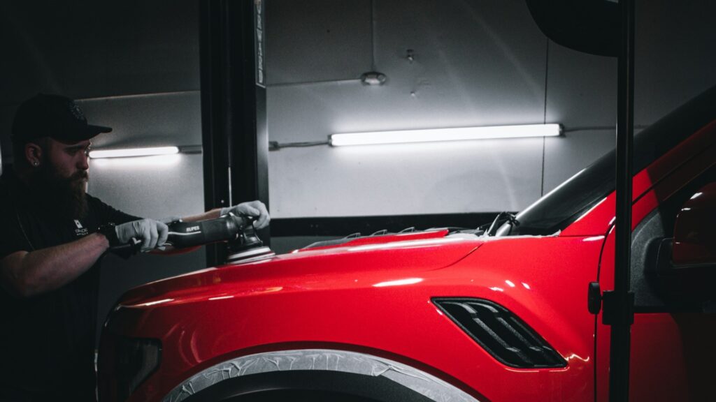 Detail specialist polijst rode auto voor perfecte afwerking van de autolak in professionele werkplaats